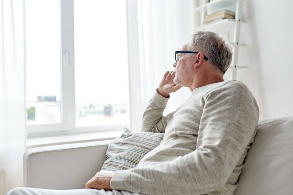 a man by himself on the couch looking wistfully out of a window