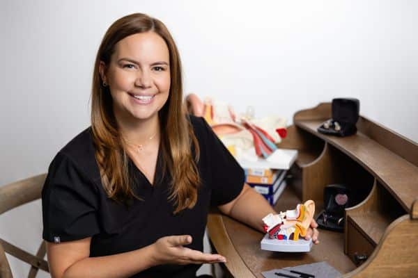 Monica smiling and pointing to a model of an ear